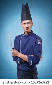 A Portrait Of An Asian Executive Chef In His Blue Uniform, Black Apron And Black Hat On Blue Background