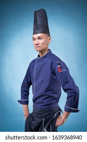 A Portrait Of An Asian Executive Chef In His Blue Uniform, Black Apron And Black Hat On Blue Background