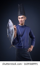 A Portrait Of An Asian Executive Chef In His Blue Uniform, Black Apron And Black Hat On Grey Background With A Skipjack Tuna