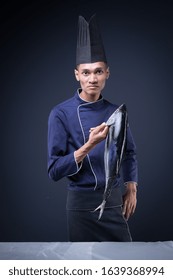 A Portrait Of An Asian Executive Chef In His Blue Uniform, Black Apron And Black Hat On Grey Background With A Skipjack Tuna