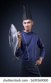 A Portrait Of An Asian Executive Chef In His Blue Uniform, Black Apron And Black Hat On Grey Background With A Skipjack Tuna