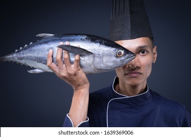 A Portrait Of An Asian Executive Chef In His Blue Uniform, Black Apron And Black Hat On Grey Background With A Skipjack Tuna