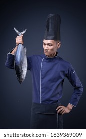 A Portrait Of An Asian Executive Chef In His Blue Uniform, Black Apron And Black Hat On Grey Background With A Skipjack Tuna