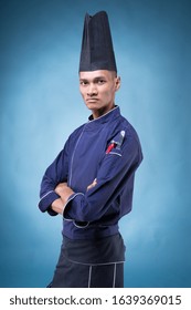 A Portrait Of An Asian Executive Chef In His Blue Uniform, Black Apron And Black Hat On Blue Background