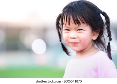 Portrait of Asian face child girl sweet smile. Happy kid with blurred bokeh background in the evening. Cute baby with black hair braided two braids on each side. Copy space.