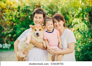 Portrait Of Asian Family (parents And Baby) Who Smiling Together With Their Dog In The Garden.