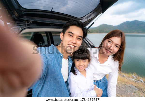 Portrait of Asian\
family sitting in car with father, mother and daughter selfie with\
lake and mountain view by smrtphone while vacation together in\
holiday. Happy family\
time.