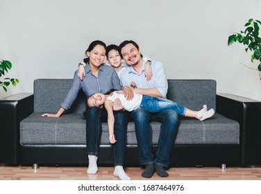 Portrait Of And Asian Family With Two Kida Sitting On A Sofa. 