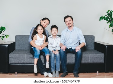 Portrait Of And Asian Family With Two Kida Sitting On A Sofa. 