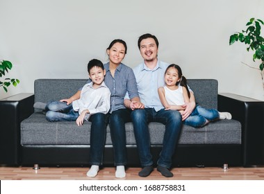 Portrait Of And Asian Family With Two Kida Sitting On A Sofa. 