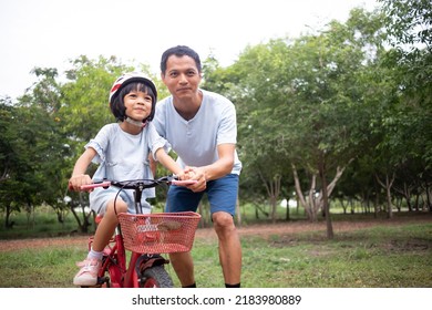 Portrait Asian Father And Daughter Father Is Training And Teaching A Daughter Who Wears A Safety Helmet. She Sits On A Red Bicycle With Her Father Taking Care Of  Closely With Concern.they Learn Happy