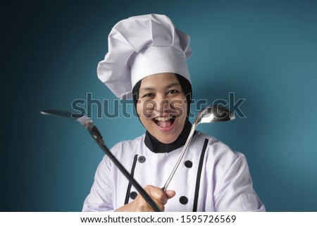 Portrait of Asian female chef shows ladle and spatula, ready to cook in the kitchen, kungfu chef in action