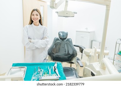 Portrait Of Asian Female Dentist Stand Cross Arm In Dental Exam Room. Attractive Young Woman Dental Doctor Standing With Confident In Dental Examination Room, Smiling And Looking At Camera At Clinic.