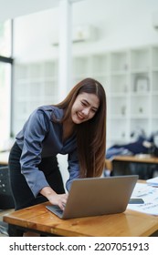 Portrait Of An Asian Female Employee Standing At A Computer With A Smiling Face As She Works The Next Morning.