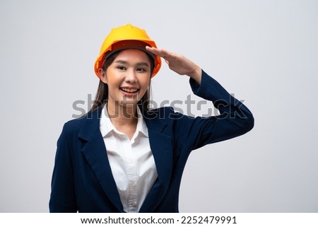 Portrait of Asian female engineer with hard hat making army salute isolated on grey background.