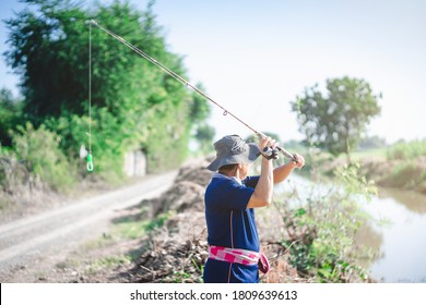 Portrait Of Asian Fisherman Catching Fish With Reel Rod And Fishing Lure Or Fake Bait At Canal .Asian Mature Man Fishing At Canal Or River.