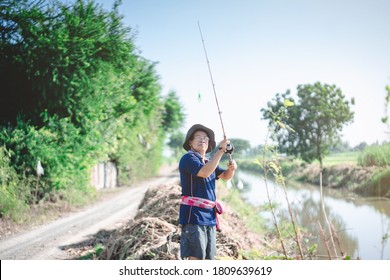 Portrait Of Asian Fisherman Catching Fish With Reel Rod And Fishing Lure Or Fake Bait At Canal .Asian Mature Man Fishing At Canal Or River.