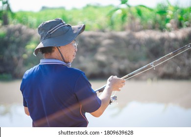 Portrait Of Asian Fisherman Catching Fish With Reel Rod And Fishing Lure Or Fake Bait At Canal .Asian Mature Man Fishing At Canal Or River.