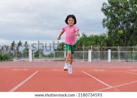 Portrait, an Asian girl aged 6 years and over, wearing a pink shirt. green pants are jogging in different poses In the red track of the stadium for healthy and have fun doing activities with  family. 
