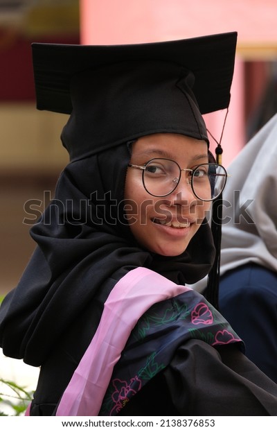 portrait of\
an Asian girl with hijab in her graduation hat holding certificate\
and showing happiness\
expression