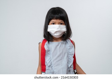 Portrait Of Asian Girl Kid With Protective Face Mask And School Backpack Ready For New School Year With Pandemic Restrictions. Concept Of Kid Going Back To School And New Normal Lifestyle