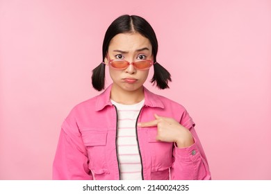 Portrait Of Asian Girl Looks Confused And Points At Herself, Perplexed Face, Stares With Disbelief At Camera, Stands Over Pink Background