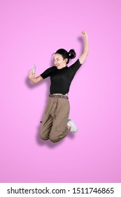 Portrait Of Asian Girl Looks Excited While Using A Mobile Phone And Jumping In The Studio