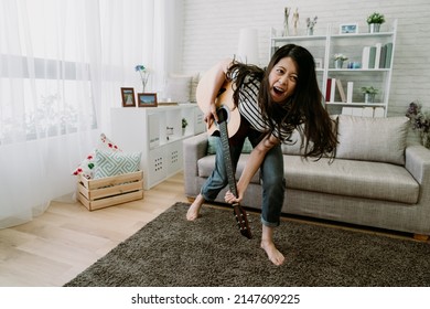 Portrait Asian Girl Playing Guitar Imagining Herself A Rocker. Taiwanese Woman Performing Music Is Bending And Leaning Forward With Fierce-looking Facial Expression. Indoor Recreation Concept.