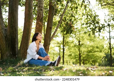 Portrait of asian girl relaxing, leaning on tree and resting in park under shade, smiling and enjoying the walk outdoors. - Powered by Shutterstock