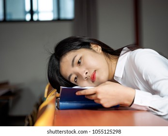 Portrait Of Asian Girl Student In School Uniform Japanese Style, Lying On School Desk Reading A Book With Blur Classroom Background.