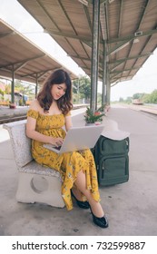 Portrait Of Asian Girl Texting On A Laptop In A Train Station While Is Waiting, Asia Woman With The Notebook On The Train Platform.