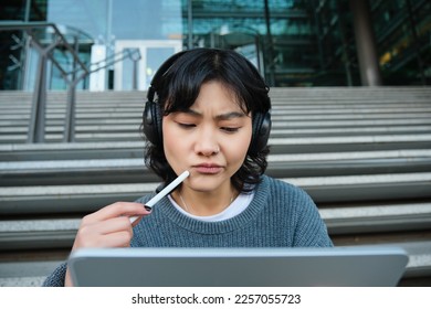 Portrait asian girl and troubled face  draws digital tablet and pen  looks complicated at her work  feels stuck no inspiration  sits stairs   thinks 