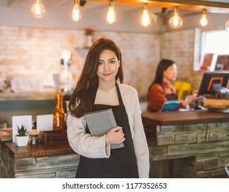 Portrait of Asian girl waitress holding menu wearing apron and standing in coffee shop.