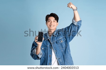 Portrait of an Asian guy wearing a jacket and using a phone posing on a blue background