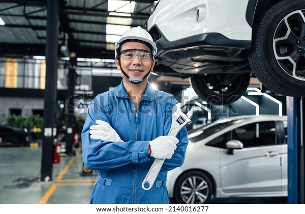 Portrait of Asian handsome automotive mechanic\
men standing in garage. Vehicle service manager worker work in\
mechanics workshop, looking at camera after check and maintenance\
to repair the engine.