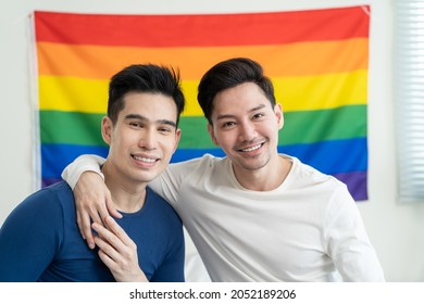 Portrait Of Asian Handsome Man Gay Family Holding LGBT Flag And Smile. Attractive Romantic Male Lgbt Couple Sit On Bed In Bedroom In Morning And Looking At Camera With Gay Pride And Rainbow Background