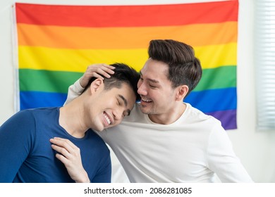 Portrait Of Asian Handsome Man Gay Family Holding LGBT Flag And Smile. Attractive Romantic Male Lgbt Couple Sit On Bed In Bedroom In Morning, Look At Each Other With Gay Pride And Rainbow Background.