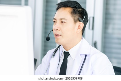 Portrait Asian handsome smart male doctor smiling with headsets, sitting and looking at computer screen, making online telemedicine, giving service, advise medicines or medical treatment to patients - Shutterstock ID 2055539909