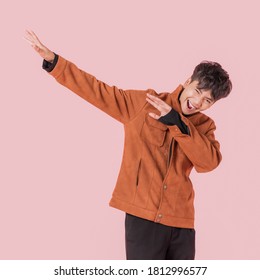 Portrait Of Asian Handsome Young Man In Fashionable Clothing And Enjoy Standing With Gesture Dab Dance Isolated On Pink Background.