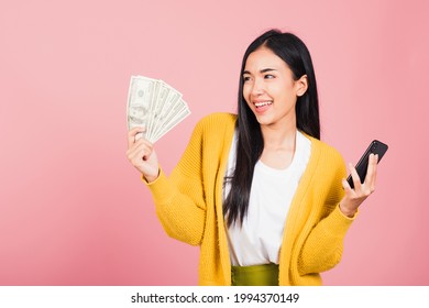 Portrait Asian Happy Beautiful Young Woman Teen Shopper Smiling Standing Excited Holding Online Smart Mobile Phone And Dollar Money Banknotes On Hand In Summer, Studio Shot Isolated On Pink Background