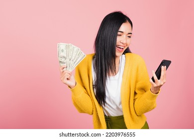 Portrait Asian happy beautiful young woman teen shopper smiling standing excited holding online smart mobile phone and dollar money banknotes on hand in summer, studio shot isolated on pink background - Shutterstock ID 2203976555