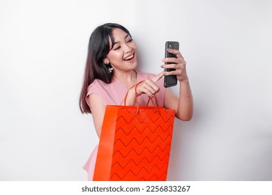 Portrait Asian happy beautiful young woman standing excited holding an online shopping bag and her smartphone, studio shot isolated on white background - Shutterstock ID 2256833267