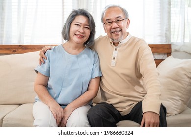 Portrait Of Asian Happy Family, Senior Elderly Couple Enjoy Retirement Life At House. Older Grandfather And Grandmother Sit On Sofa And Smiling, Looking At Camera At Home. Health Care Activity Concept