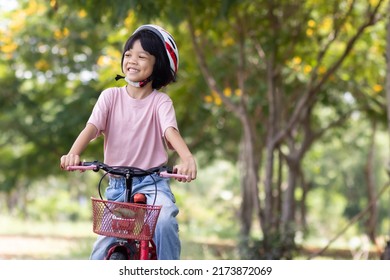 Portrait Of An Asian Kid Girl With A Cute Face Wearing A Helmet. Ride On Her Favorite Red Bike. With A Happy Smiling Face Who Went Out To Ride A Bike To Exercise In The Morning In The Health Park.