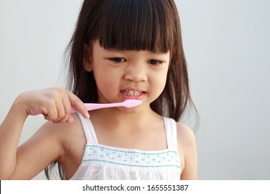 Portrait Asian Kid Girls Aged 4 To 6 Years, Long Hair Wearing A White Shirt Pretty Face Happily Brushing His Teeth The Hand Holds A Pink Toothbrush.Brushing Teeth Makes Her Teeth Strong.