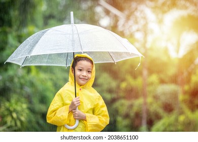 Portrait Asian Kid Holding An Umbrella With Raindrops. Happy Asian Little Child Boy Having Fun Playing With The Rain In The Evening Sunlight.