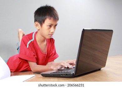 Portrait Of Asian Kid Laying On The Floor Using Laptop On Grey Background