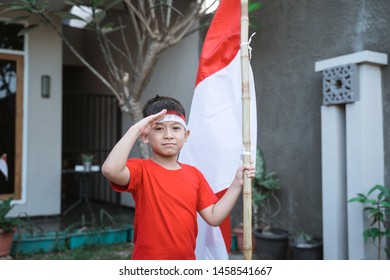 Portrait Of Asian Kid Saluting While Holding Indonesia Flag