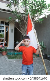 Portrait Of Asian Kid Saluting While Holding Indonesia Flag