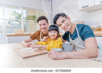 Portrait Of Asian LGBTQ Man Gay Family Make Bake With Girl In Kitchen. Attractive Handsome Male Couple Spending Time With Little Cute Child Baking Bakery Together, Enjoying Parenting Activity At Home.